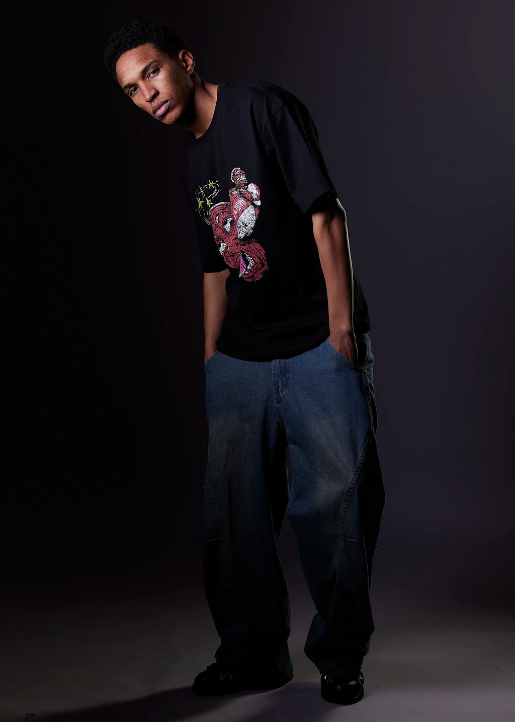 Person wearing a black t-shirt with a graphic design and blue jeans against a dark background