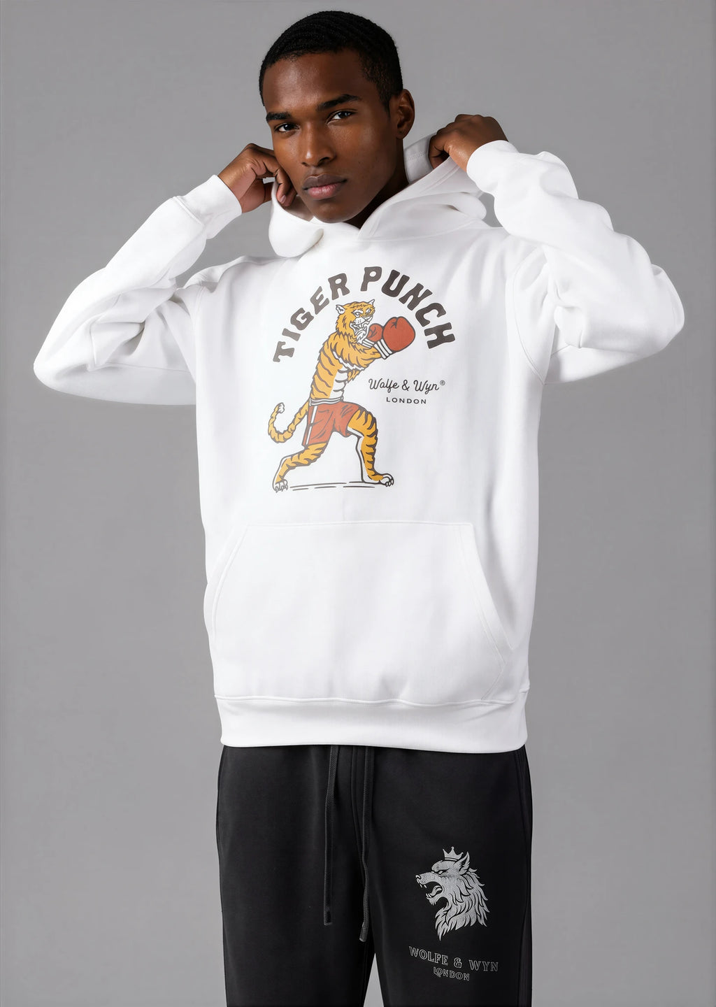 Person wearing a white hoodie with a tiger graphic and text, standing against a gray background