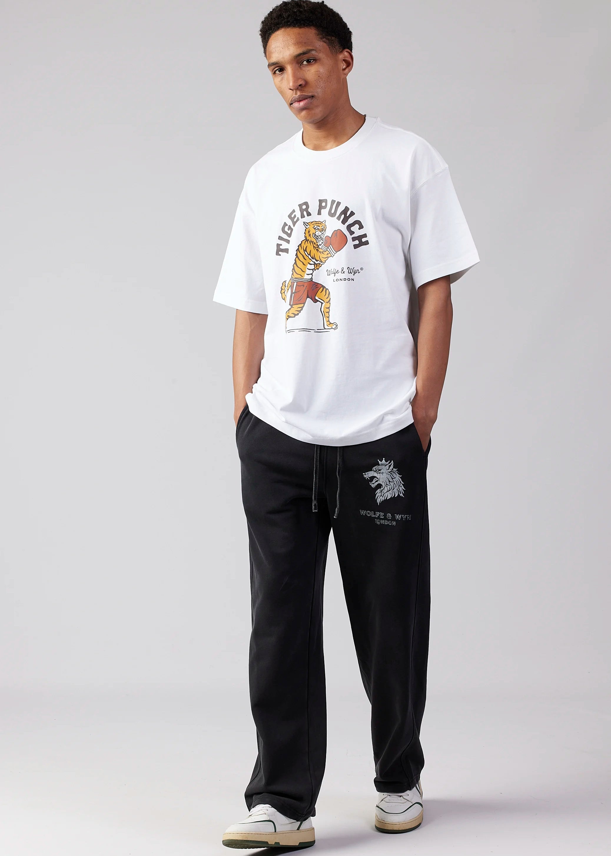 Person wearing a white t-shirt with a graphic design and black pants on a gray background