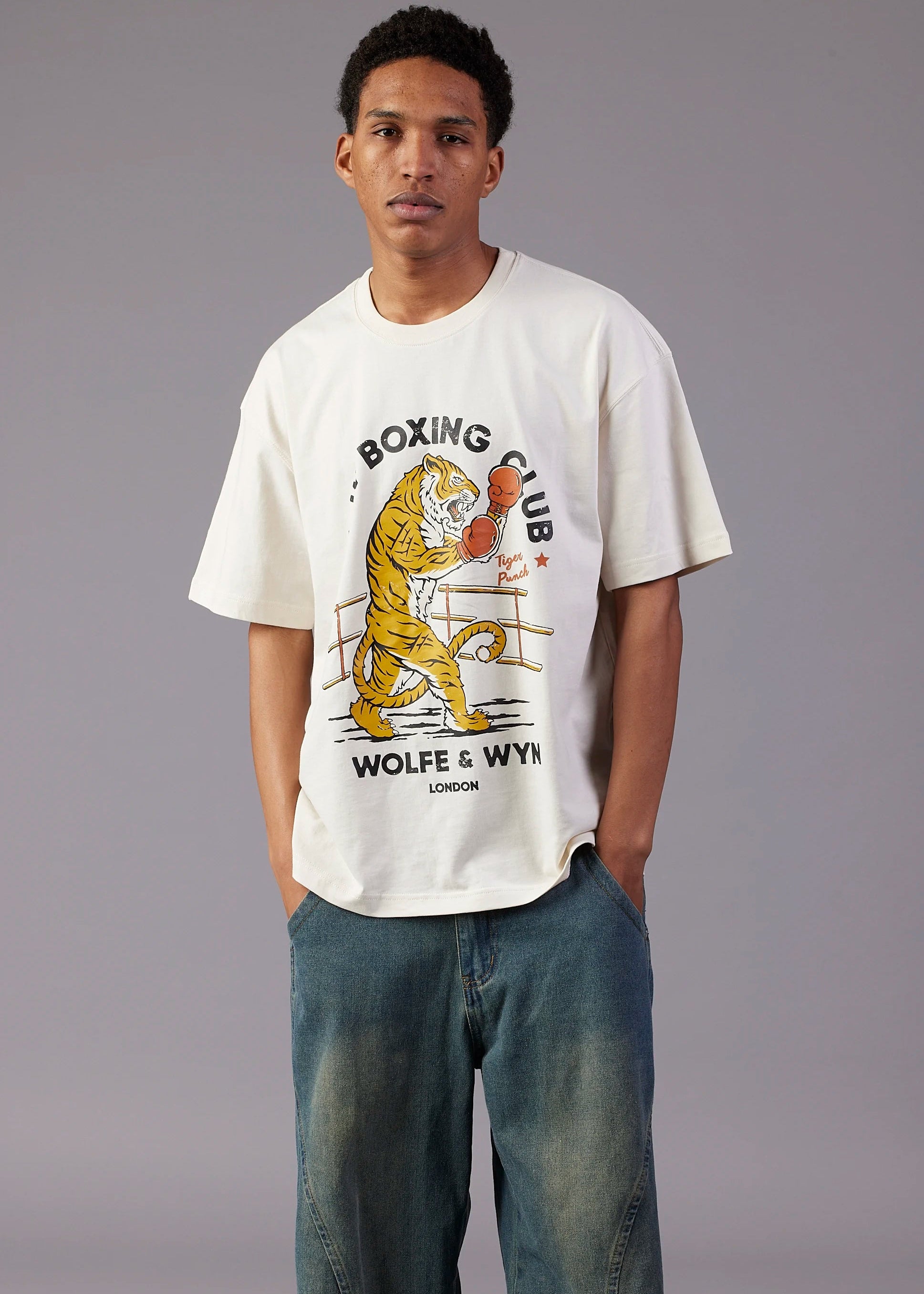 Man wearing a white t-shirt with a tiger graphic and text, standing against a gray background